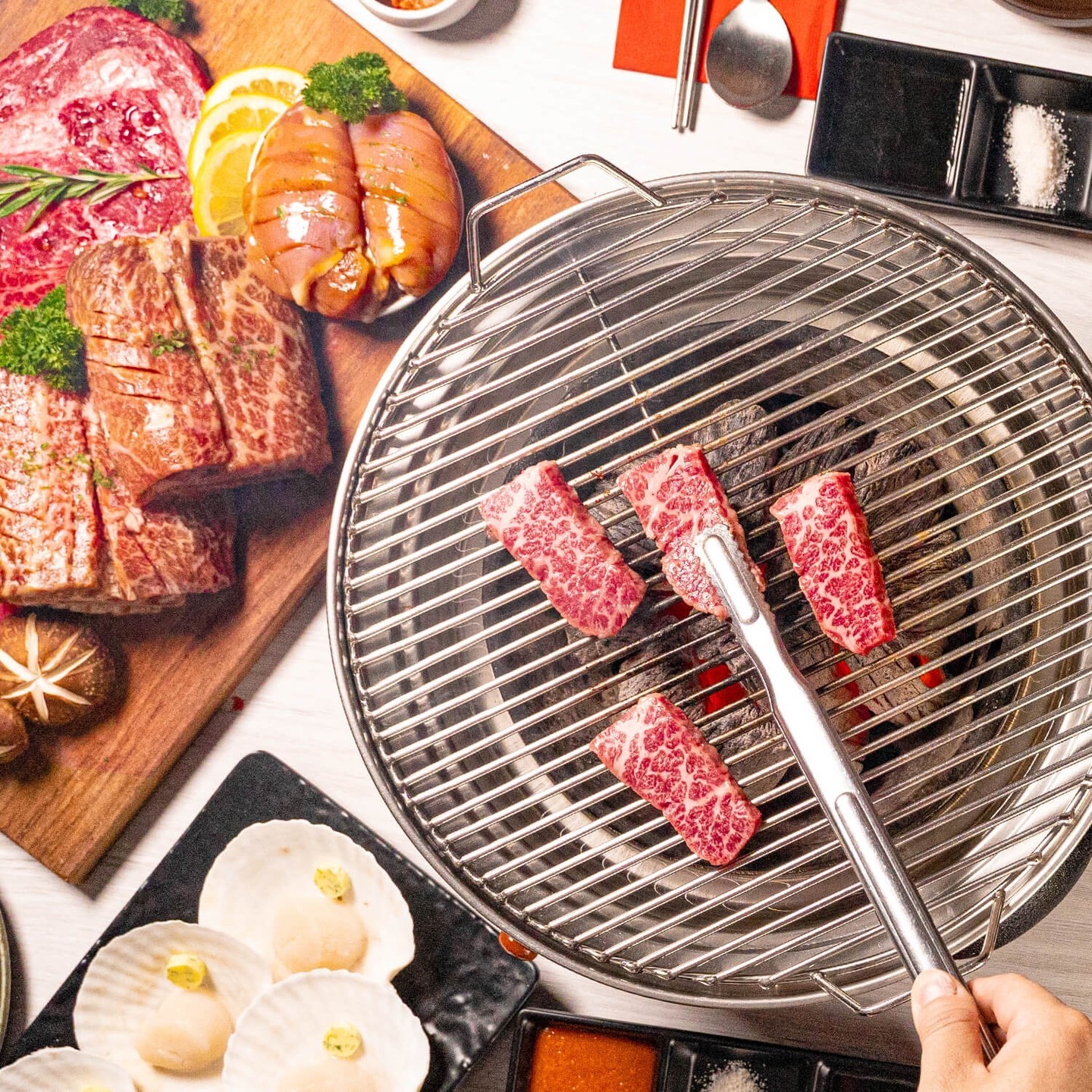 Premium beef cuts beside a charcoal grill with tongs searing wagyu